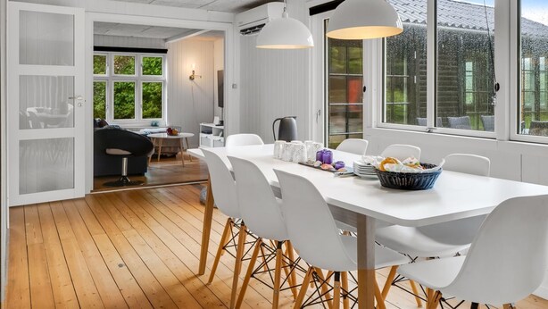 Un comedor moderno con una mesa y sillas blancas, un ventanal con vistas a la vegetación y un techo con un diseño original.