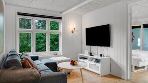 Una sala moderna con un televisor grande, un sofá, una mesa de centro y una ventana con vista a zonas verdes.