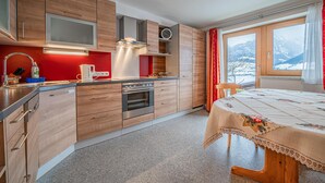 A modern kitchen with wooden cabinets, a built-in oven, and a window with a mountain view. - Beautiful holiday apartment in Niedernsill (Niedernsill)