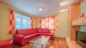 A living room with a red sectional sofa, a glass coffee table, wooden flooring, and a wooden cabinet with a TV. - Beautiful holiday apartment in Niedernsill (Niedernsill)