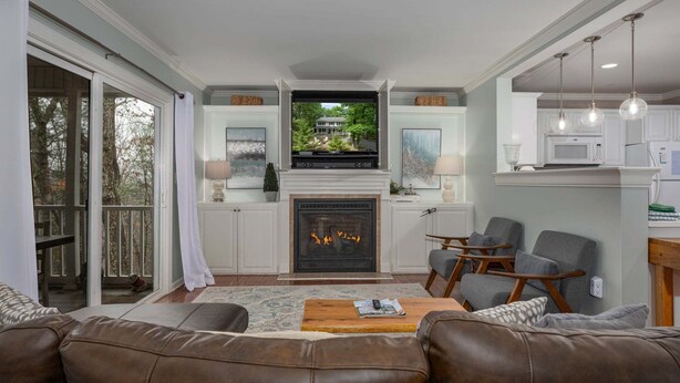 A living room with a fireplace, a television, and a view of a house through a sliding door. - On The Rocks! Spacious family-friendly 4BR home w/ bonus room (Basye)