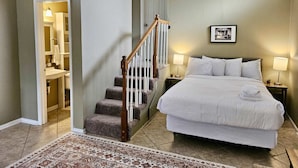 A bedroom with a large bed, a wooden staircase, a bathroom with a sink and mirror, and a framed picture on the wall. - Pool & Mins to Zoo - Capitol Heights Hideaway (Montgomery)