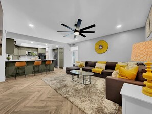 Eine moderne Küche mit einer zentralen Kochinsel, ein Essbereich mit einem runden Tisch und ein Wohnzimmer mit einer Couch und einem Couchtisch.