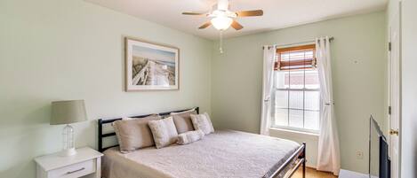 A bedroom with a bed, nightstand, ceiling fan, window with curtains, and a TV.