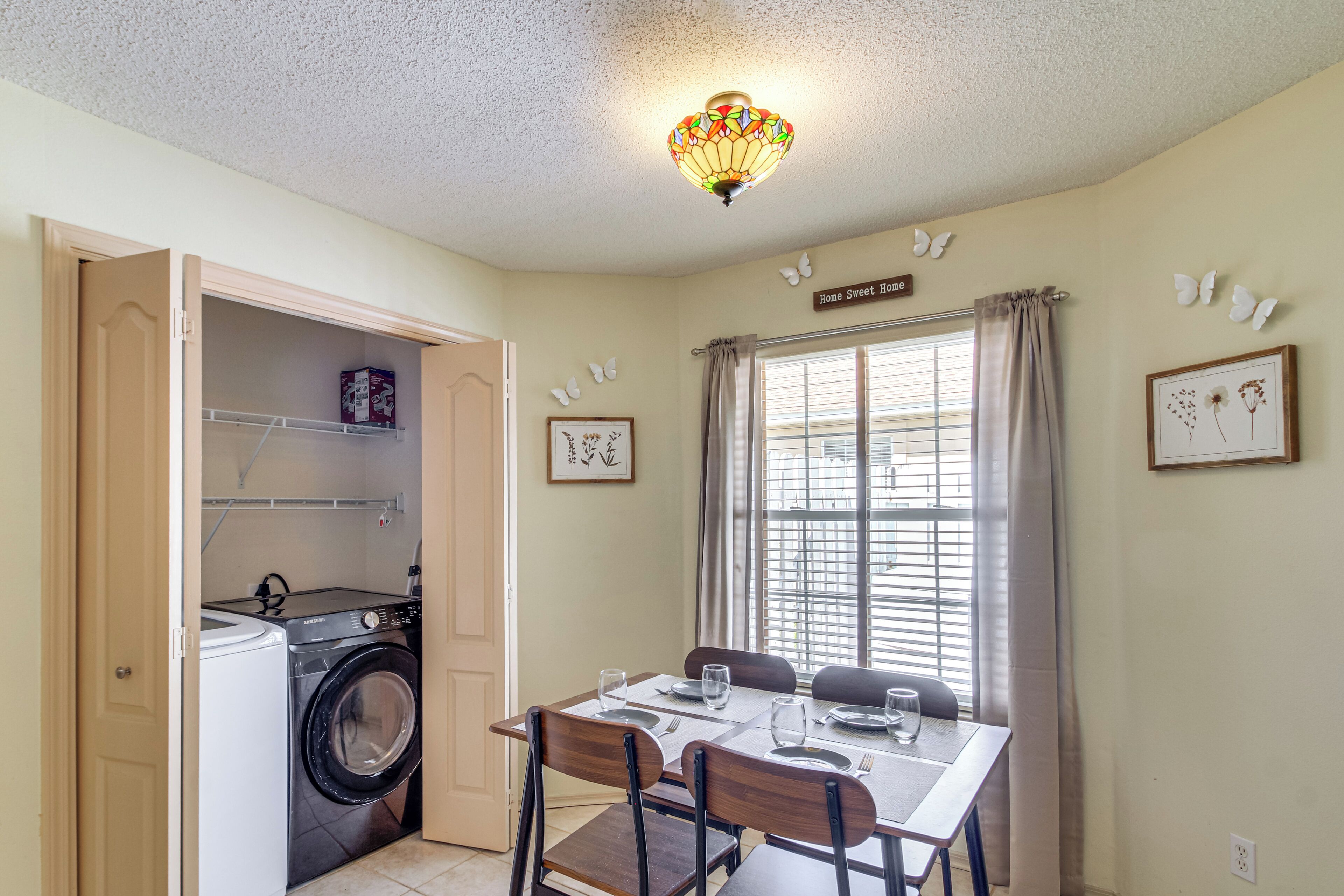 Een eetgedeelte met een tafel voor vier personen, een wasmachine in de aangrenzende kamer en een decoratieve plafondlamp.