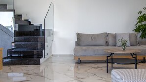 Un salon moderne avec un sol en marbre, un canapé gris, une table basse et un escalier doté de rampes en verre.