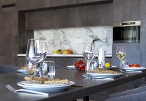 Une cuisine moderne avec un dosseret en marbre, une table à manger dressée avec des assiettes, des verres et un saladier rempli de tomates.