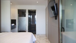 Une chambre d’hôtel moderne avec un grand lit, un téléviseur fixé au mur et une douche à parois de verre.
