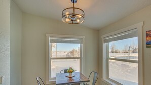A dining area with a wooden table and metal chairs, a vase with flowers, and a view of a parking lot through large windows. - Modern Bloomington Home ~ 10 Mi to Bear Lake! (Bloomington)