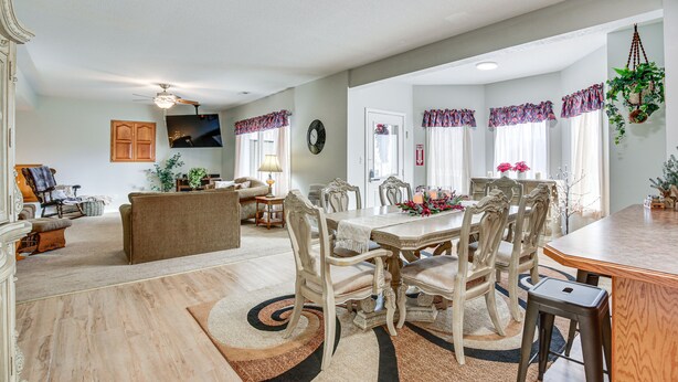 A spacious living room with a dining area, featuring a large wooden table, elegant chairs, and a chandelier.