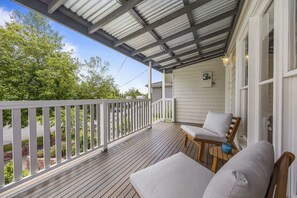 A covered porch with a white railing, a wooden bench, and a table with cushions.