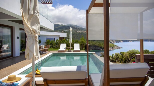 Zona de piscina moderna al aire libre con sillones de descanso y sombrillas, con vistas a un paisaje costero pintoresco.