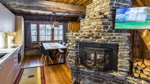 L’intérieur chaleureux d’un chalet avec une cheminée en pierre, une table à manger en bois et une grande fenêtre donnant sur un paysage enneigé.