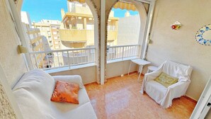 A balcony with a white sofa and chair, a small table, and a view of buildings.