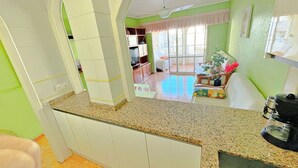 A kitchen with white cabinets, a granite countertop, and a ceiling fan. There is a dining area with a table and chairs, and a window with curtains.