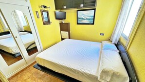 A compact hotel room with a single bed, a television, a framed picture on the wall, and a mirror.