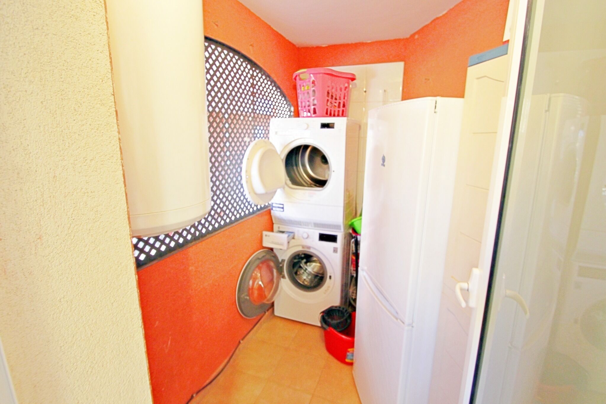 Pequeño cuarto de lavandería con lavadora, secadora y un refrigerador.