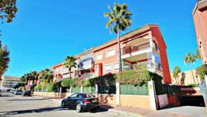 Un immeuble résidentiel à plusieurs étages, doté de balcons, de palmiers et d’une entrée sécurisée par un portail.