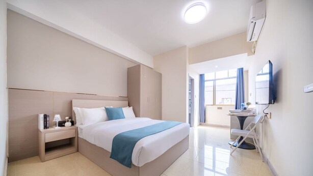 A modern hotel room with a large bed, bedside table, and a TV. - Moon Hotel Apartment Guangzhou Baijiang (Guangzhou)