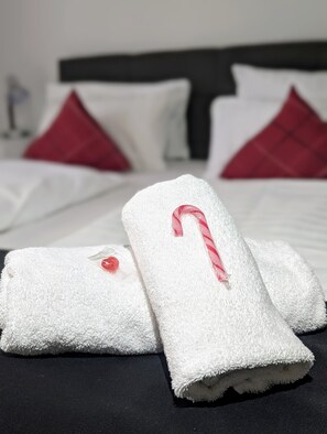 A neatly made bed with white and red pillows, a white towel with a candy cane, and a red button. - Room in Guest Room - City Hotel - Double Room 117 (Rastatt)