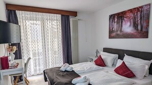 A hotel room with a large bed, a desk with a chair, a TV, and a painting on the wall. - Room in Guest Room - City Hotel - Double Room 117 (Rastatt)