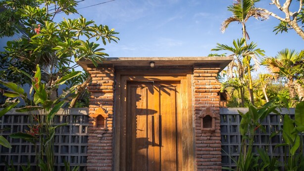 A wooden door with a brick archway, surrounded by lush greenery and a clear sky.