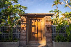 A wooden door with a brick archway, surrounded by lush greenery and a clear sky. - VILLA KOMANG JIMBARAN (Jimbaran)