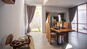 A modern dining area with a wooden table and chairs, a large window with curtains, and a view of a garden.
