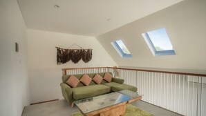 A spacious loft with a green sofa, a glass coffee table, and a view of the sky through skylights.