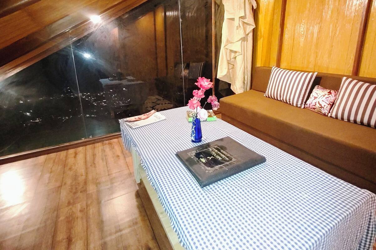 Ein gemütliches Zimmer mit Holzbalkendecke, einem karierten Tisch, einer Couch mit gestreiften Kissen und einer Vase mit Blumen.