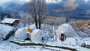 A snow-covered village with geodesic dome structures, a stone wall, and a view of a valley with mountains in the background. - Nirvana Hamta Retreat (Manali)