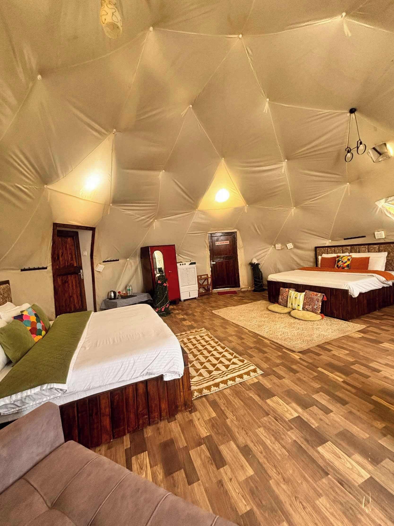 A spacious tent-style room with two beds, a sofa, and a small table.