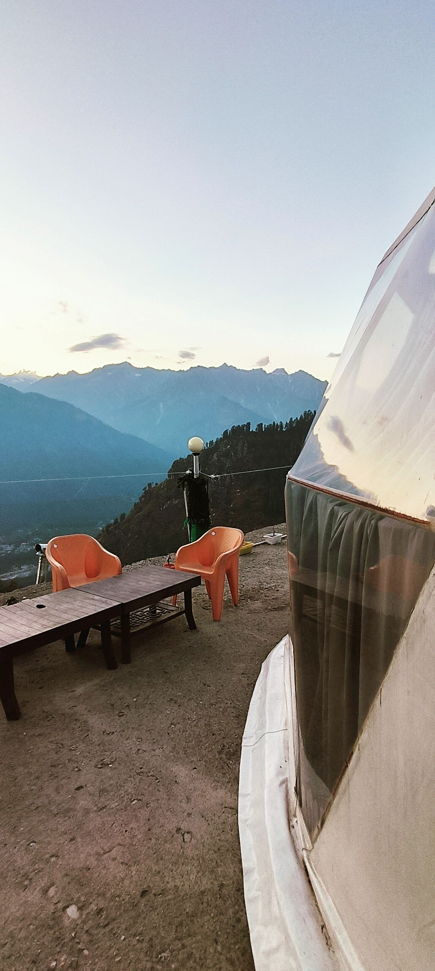 A tent with a table and two chairs set up on a hillside overlooking a mountainous landscape.