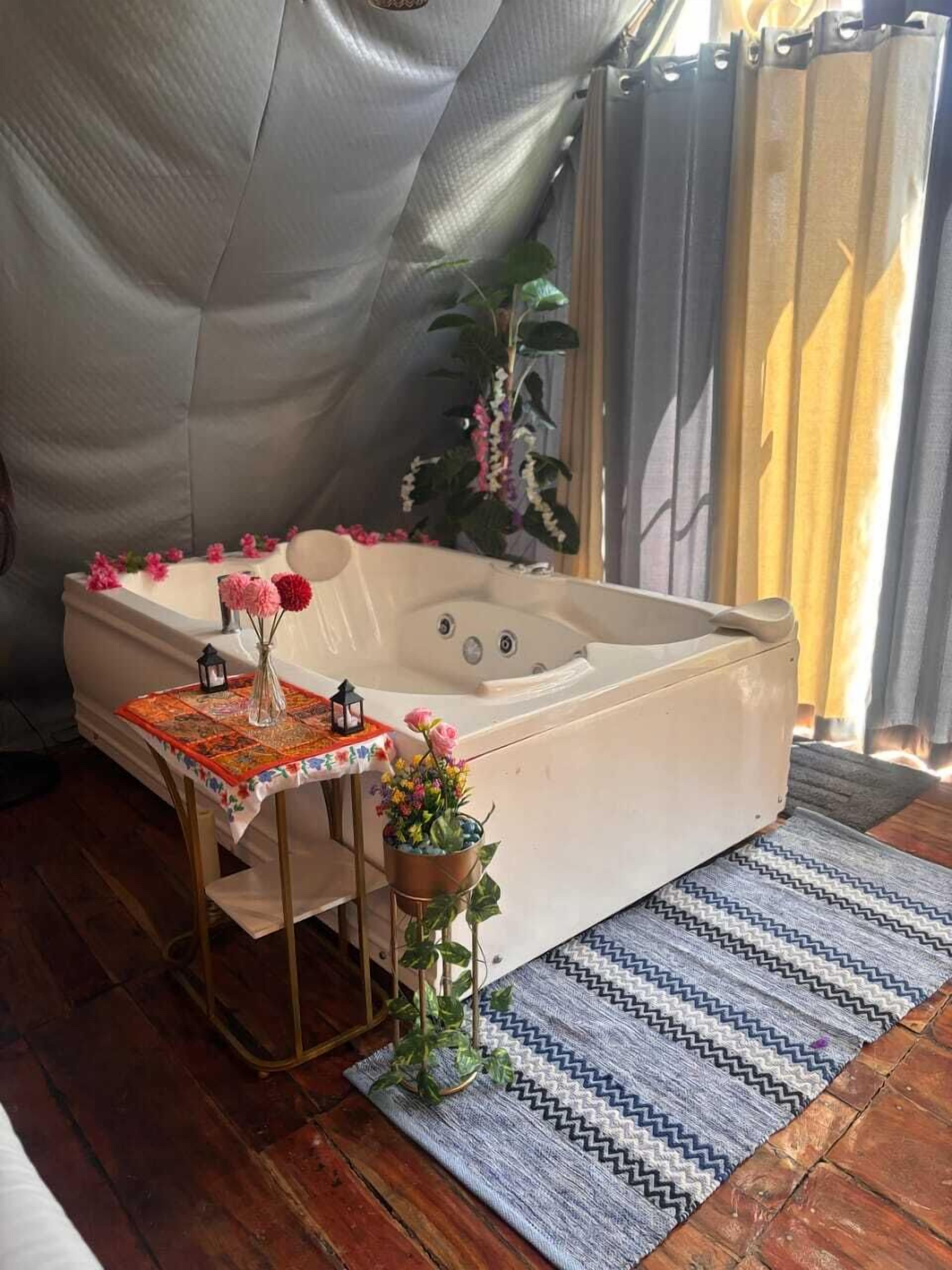 A cozy room with a large bathtub, a small table with a quilt, and a potted plant.