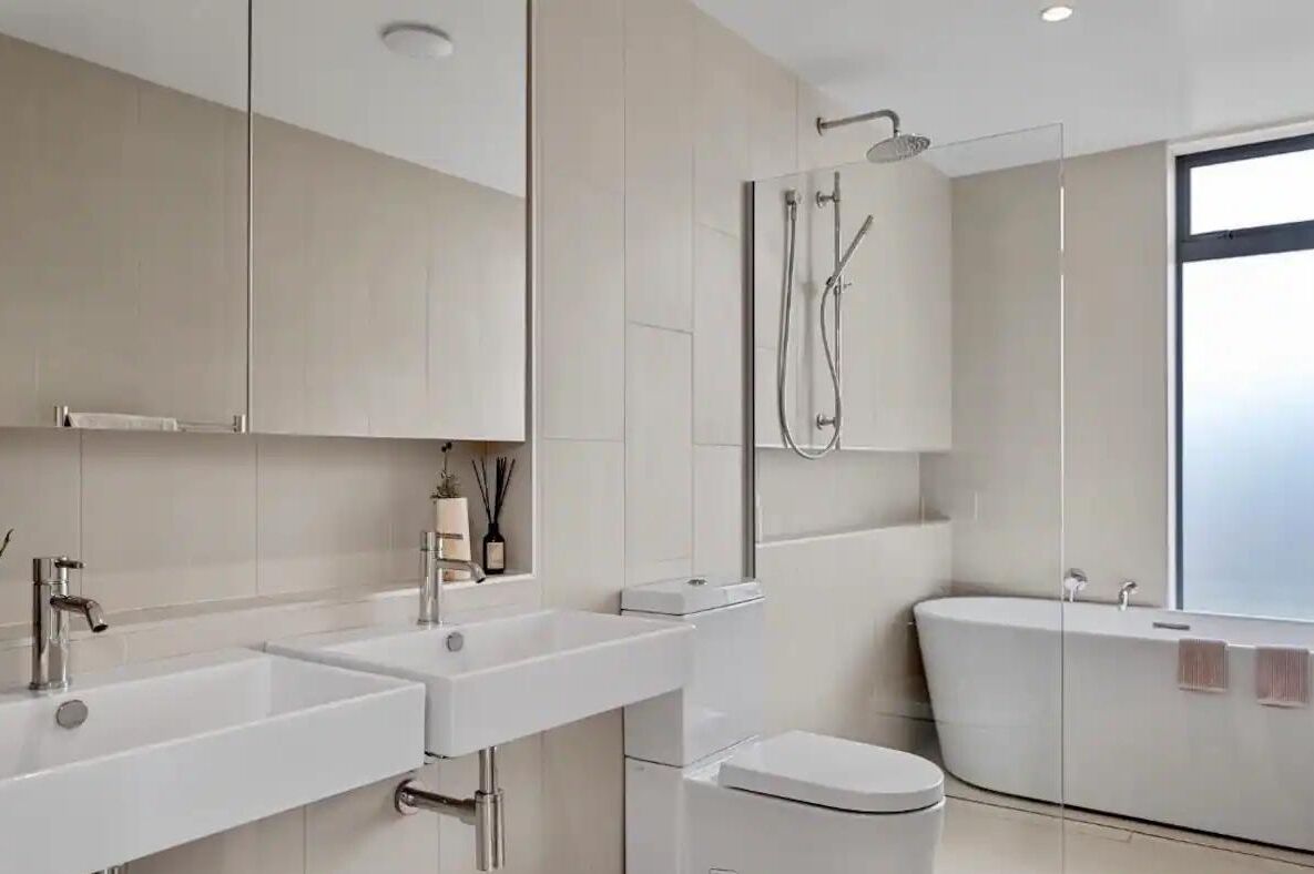 A modern bathroom with two sinks, a toilet, and a bathtub.
