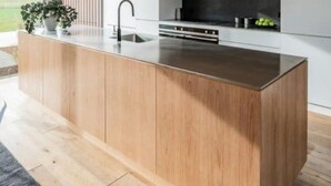 A modern kitchen with a large island, wooden cabinets, and a black backsplash. - Te Whare Waipara

 (Broomfield)