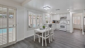 A modern kitchen with white cabinetry, a dining area with a table and chairs, and a view of a swimming pool through the windows.