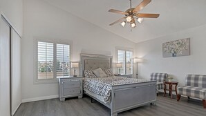 A bedroom with a bed, two bedside tables, a ceiling fan, and two chairs.