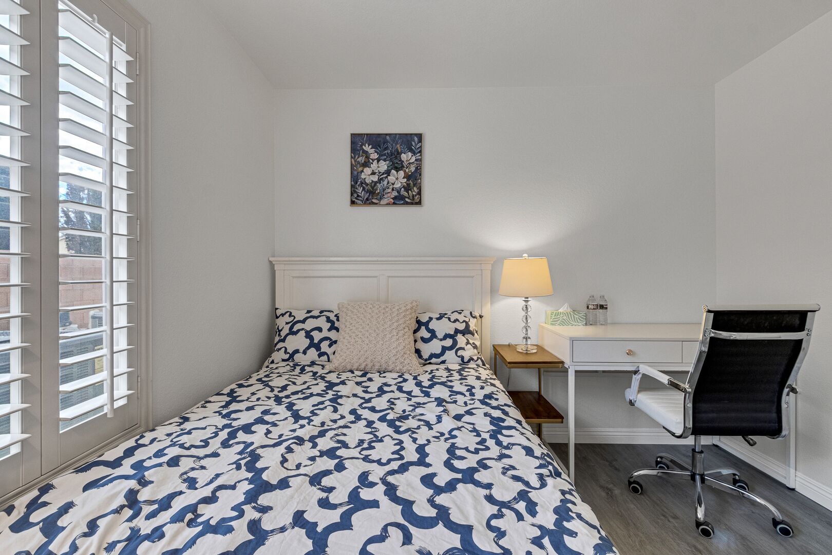 Une chambre à coucher avec un lit, un bureau, une chaise, une lampe et un tableau au mur.