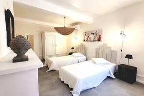 A hotel room with two beds, a wardrobe, a mirror, a painting, and a decorative fruit bowl.