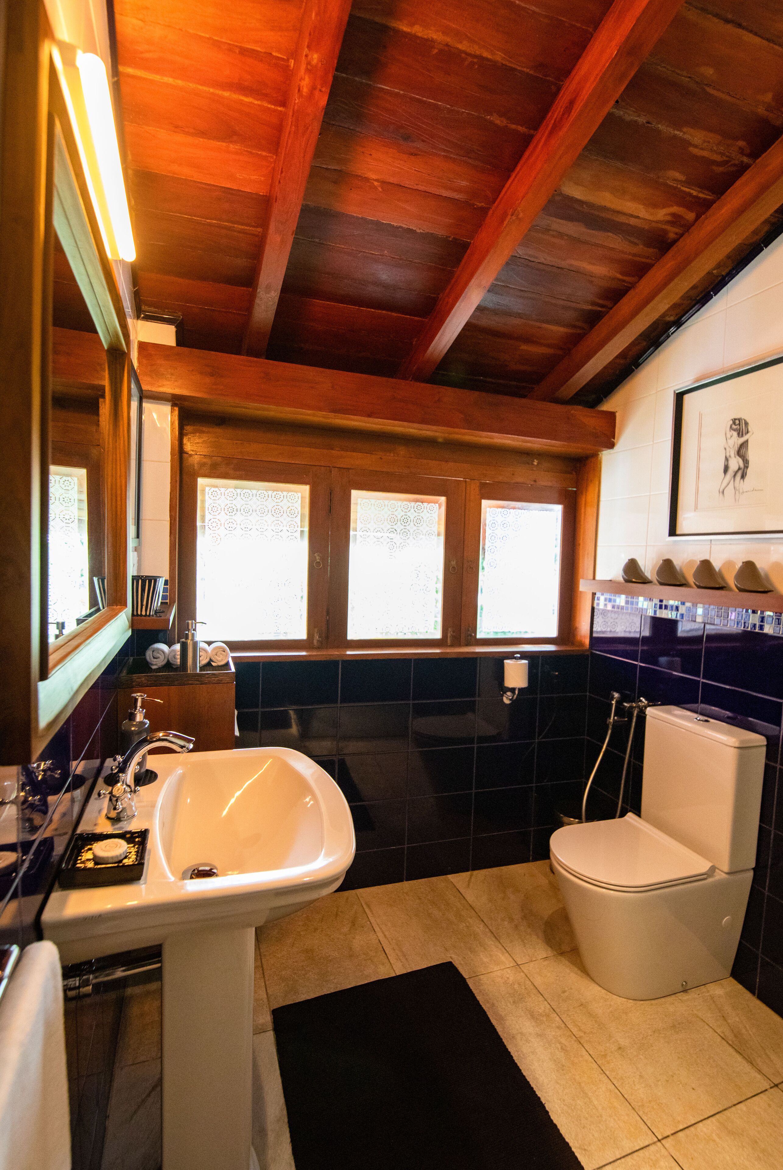 A bathroom with a wooden ceiling, a sink, a toilet, and a window with patterned glass.