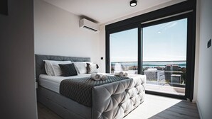 A modern bedroom with a large bed, a view of the city through a sliding glass door, and an air conditioning unit on the wall. - Villa `Just be Happy` by Trawelltopia | Heated Whirl/-Pool · View · AC · WIFI · Parking (Kaštel Stari)