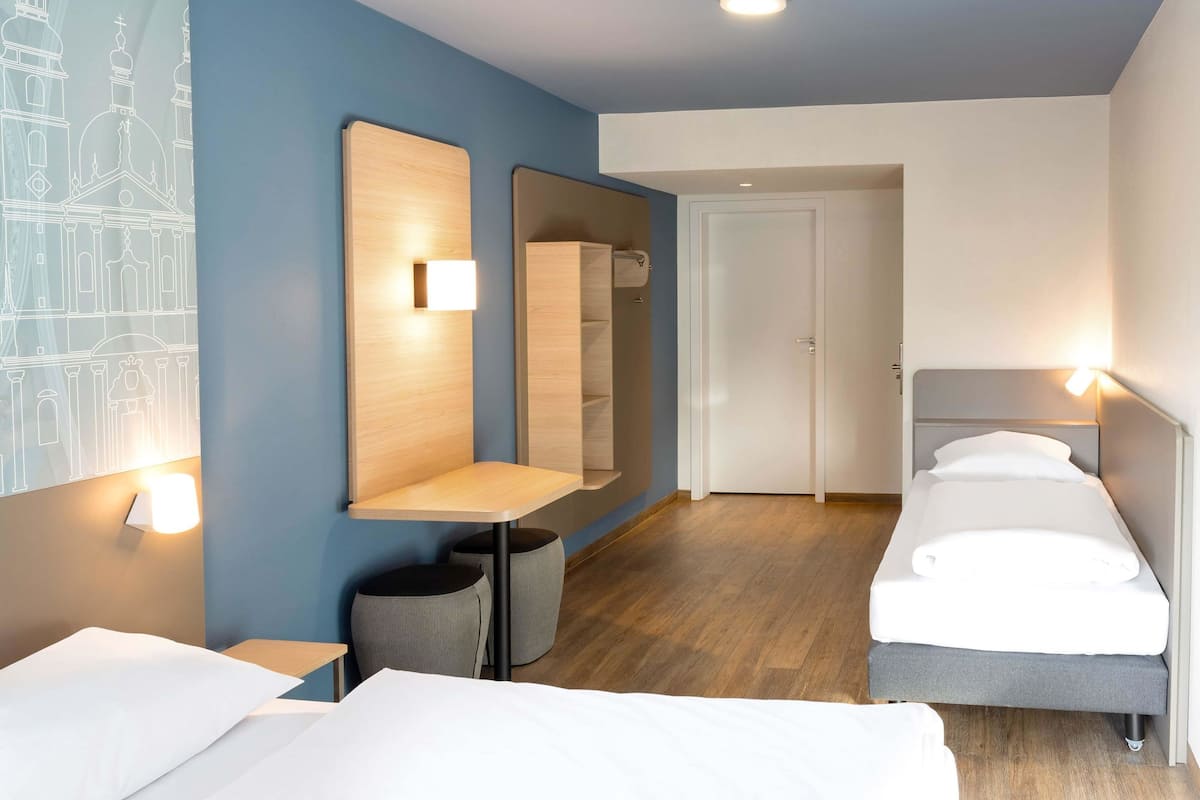 A hotel room with two beds, a wooden desk, a mirror, and a wardrobe.