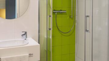 Un baño con lavamanos blanco, un espejo y una ducha con azulejos verdes.