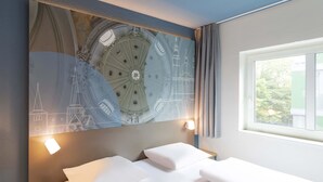 Habitación de hotel con un gran mural en la pared de una torre del reloj, una cama con sábanas blancas, una mesita de noche y una ventana con cortinas.