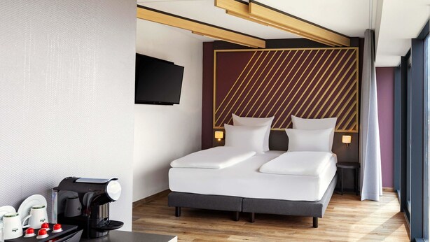 Ein modernes Hotelzimmer mit Bett, Nachttischen, einer Kaffeemaschine und einem an der Wand befestigten Fernseher.