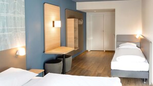 Ein Hotelzimmer mit zwei Betten, einem Holztisch, einem Spiegel und einem Kleiderschrank.