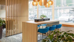 Ein moderner Empfangsbereich mit einem Holztisch, blauen Barhocker und einer Topfpflanze.