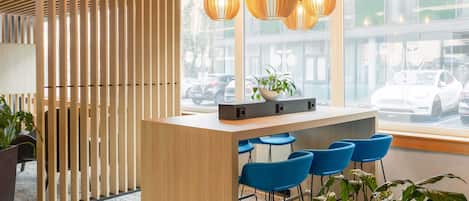 Uma área de recepção moderna com uma mesa de madeira, banquetas azuis e um vaso de planta.