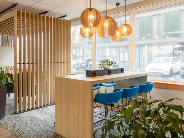 Una zona de recepción moderna con un mostrador de madera, taburetes azules y una planta en maceta.